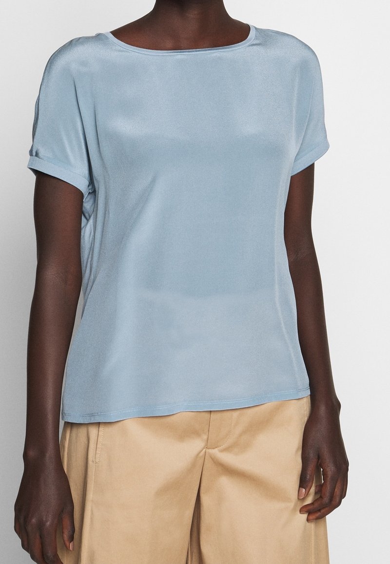 Haut bleu clair à manches courtes avec une texture douce et lisse et un large décolleté. Il présente des manches retroussées et une coupe décontractée, associé à un pantalon beige.