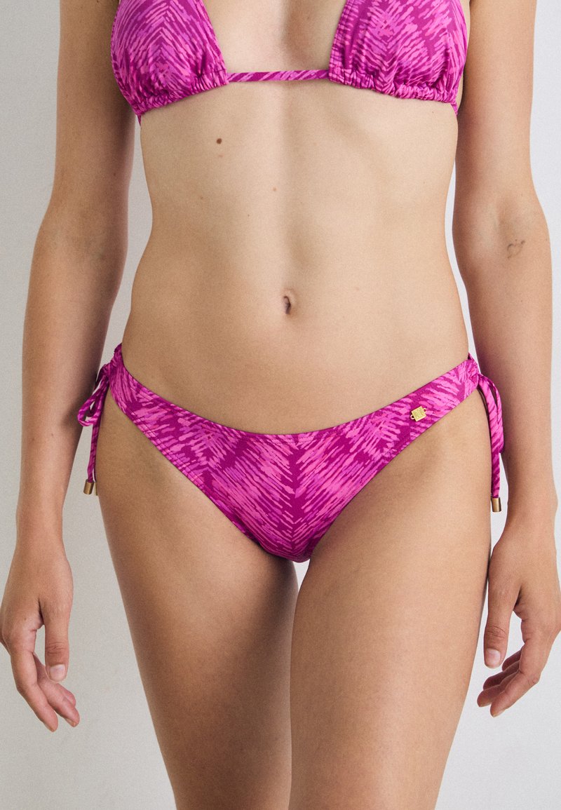 Bikini set u svijetloj ružičastoj boji s cik-cak uzorkom. Ima trokutasti gornji dio i donji dio sa vezicama sa zlatnim detaljima na vezicama. Glatka tekstura.