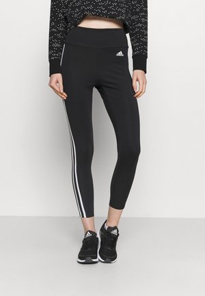 Leggings de sport noirs avec une taille haute, ornés de bandes blanches à trois rayures sur les côtés, fabriqués en tissu extensible.