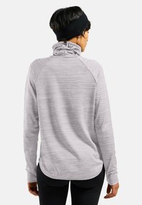 Lichtgrijze langekleding top met een hoge kraag, gestructureerd patroon en raglanmouwen. Beschikt over een gebogen zoom en verstelbare halsafsluiting.