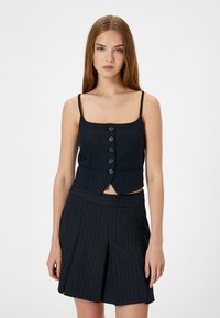 Top cropped a righe blu navy con bottoni e spalline sottili, abbinato a una gonna plissettata coordinata con una vita larga.
