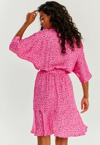 Růžové šaty krátkého rukávu s volným střihem a vzorem červených skvrn. Mají elastický pas a rozšířený spodní lem, vyrobené z lehkého materiálu.