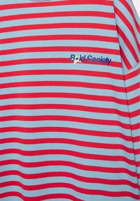 Rot- und hellblau gestreiftes horizontales Hemd mit dem Text "Bold Society" und einem Sternmotiv auf der linken Brustseite.