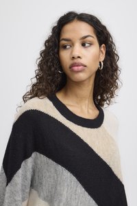 Pull en tricot avec des rayures angulaires beige, noir et gris. Encolure ronde avec bord-côte et coupe décontractée. Texture douce et légère.