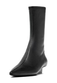 Stivale alla caviglia in pelle nera con punta affusolata e tacco basso e affusolato. Presenta una texture liscia e raffinata con dettagli di cucitura minimi.