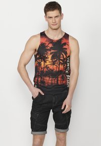 Fekete ujjatlan felső narancssárga naplementét és pálmafát ábrázoló mintával, az oldalán "Venice Beach" felirattal. Sötétkék farmer rövidnadrággal viselt.