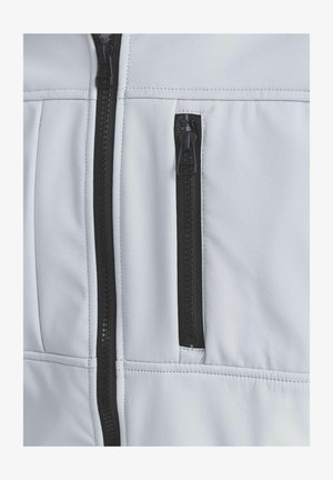 Biela textilná bunda s čiernym zipsom, textúrovaným povrchom a malou vreckou na zips na hrudi. Švy sú viditeľné.