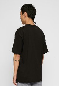 Crni oversize T-shirt izrađen od pamuka; ima okrugli izrez i široke rukave; prikazan s leđa bez uzoraka ili grafike.