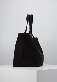 Black canvas tote bag with two long handles, featuring a minimalist design, smooth texture, and side stitching detail.