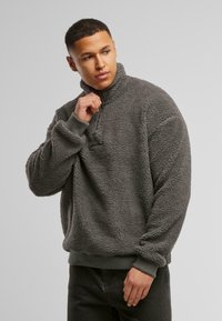 Grå fleece-pullover med høy krage, ribbestrikkede mansjetter og nederste kant. Myk, teksturert overflate med en avslappet passform og lomme-detalj.