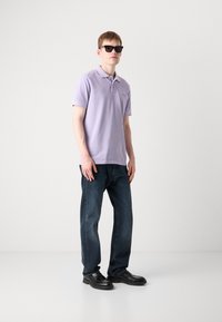 Lyselilla polo skjorte, korte ermer og krage; mørke denim jeans; svarte solbriller; solide teksturer; avslappet passform.