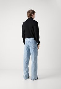 Black long-sleeve, high-neck top paired with light blue, relaxed-fit jeans, featuring a classic five-pocket design and a slight fade.