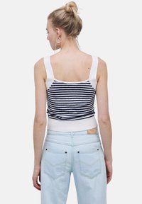 Top corto de punto a rayas en azul marino y blanco, con tirantes anchos y una cinturilla acanalada ajustada, combinado con pantalones vaqueros de tiro alto en azul claro.