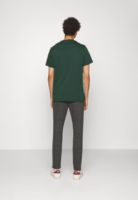 Ciemnozielona bawełniana koszulka z krótkimi rękawami, zestawiona z szarymi zwężanymi spodniami. Białe trampki z czerwonym logo na pięcie.