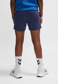 Mörkblå bomullsshorts med en jämn yta. Kombinerade med vita träningsskor och vita strumpor med svart chevronmönster.