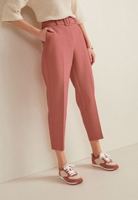 Pantalons rose à taille haute, jambes droites, et poches latérales, assortis à des baskets crème et rouge avec des lacets blancs.