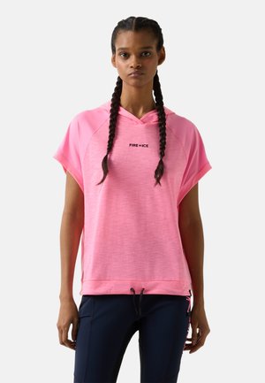 Vrouw met gevlochten haar die een felroze korte mouwen hoodie draagt met de tekst "FIRE+ICE" en donkerblauwe broek tegen een effen achtergrond.