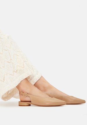 Zapatos slingback de piel beige con puntera fina, tacón corto y un detalle de hebilla redonda. Combinados con una prenda blanca de encaje.