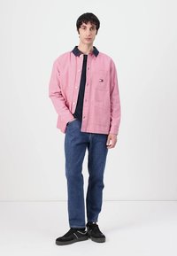 Rosa bomulljakke med mørk denimkrage, frontknapper og lomme-detaljer, kombinert med blå jeans og svarte joggesko.