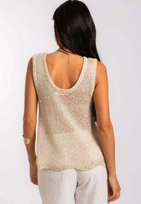 Top en tricot sans manches de couleur beige avec un large dos décoleté. Présente une texture lâche et des paillettes subtiles, terminé par un ourlet arrondi.