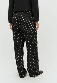 Čierne nohavice s bielymi bodkami z hladkého materiálu. Voľný strih s asymetrickým lemom, kombinované s priliehavým čiernym sako.