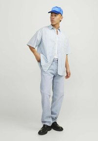 Lichtblauw gestreept overhemd met korte mouwen over een wit T-shirt, gecombineerd met lichtblauwe jeans en zwarte schoenen, afgewerkt met een blauwe pet.