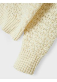 Beige gestrickter Pulloverärmel mit einem strukturierten Muster aus Schlaufen und gerippten Bündchen. Weiches Garn mit leicht flauschiger Oberfläche.