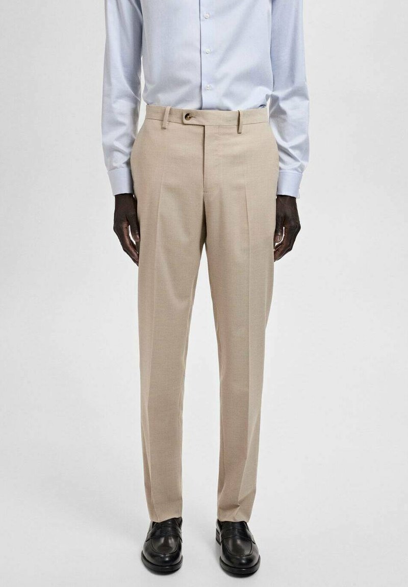 Beige dress pants with sharp creases, tailored fit, belt loops, and a smooth texture. Paired with a light blue button-up shirt and black shoes.
