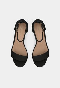 Mustat avonaiset sandaalit leveillä hihnoilla ja solk yksityiskohdalla. Liukas pinta ja beige pohja, minimalistinen muotoilu.