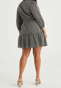 Vestido a rayas en blanco y negro con mangas tres cuartos, dobladillo con volantes y detalle de cinturón atado. Llevado con sandalias de tacón bloque.