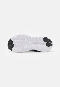 Vista inferior de una zapatilla con una entresuela blanca que presenta patrones hexagonales, acentos de suela exterior de goma negra y una textura suave.