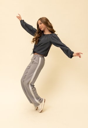 Donkerblauwe blouse met witte stippen, pofmouwen en trekkoord, gecombineerd met grijze joggerbroek met witte zijstrepen en witte sneakers.