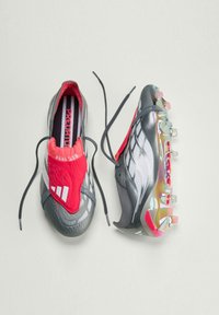 Fodboldstøvler med et gråt og rødt design, der har en tekstureret overdel, snørebånd og flerfarvede knopper under foden.