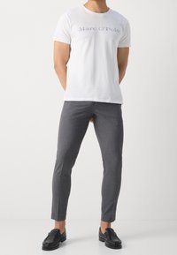 White cotton t-shirt with "Marc O'Polo" logo, paired with fitted gray fabric trousers and black leather loafers with decorative stitching.