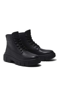 Black leather ankle boots with a padded collar, round toe, and thick rubber sole with ridges. Features metal eyelets and laces.