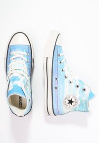 Modré a bílé ties-dye vysoké tenisky Converse All Star s bílými tkaničkami a gumovými podrážkami na bílém pozadí.