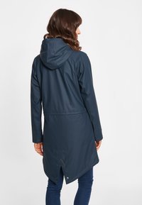 Giacca impermeabile blu navy con cappuccio, maniche lunghe e vita con cordino; presenta un orlo angolato e chiusure a snap sul retro.