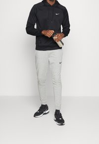 Sudadera negra con capucha y logotipo, pantalones deportivos grises con logotipo y zapatillas negras. El conjunto presenta un ajuste relajado y texturas suaves.