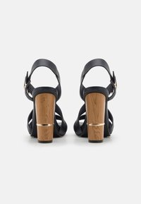 Mustat nahka sandaalit korkokengillä, avonaisella takana, säädettävällä hihnalla ja puu-blokki korkokengällä, jossa on kultainen korostusnauha.