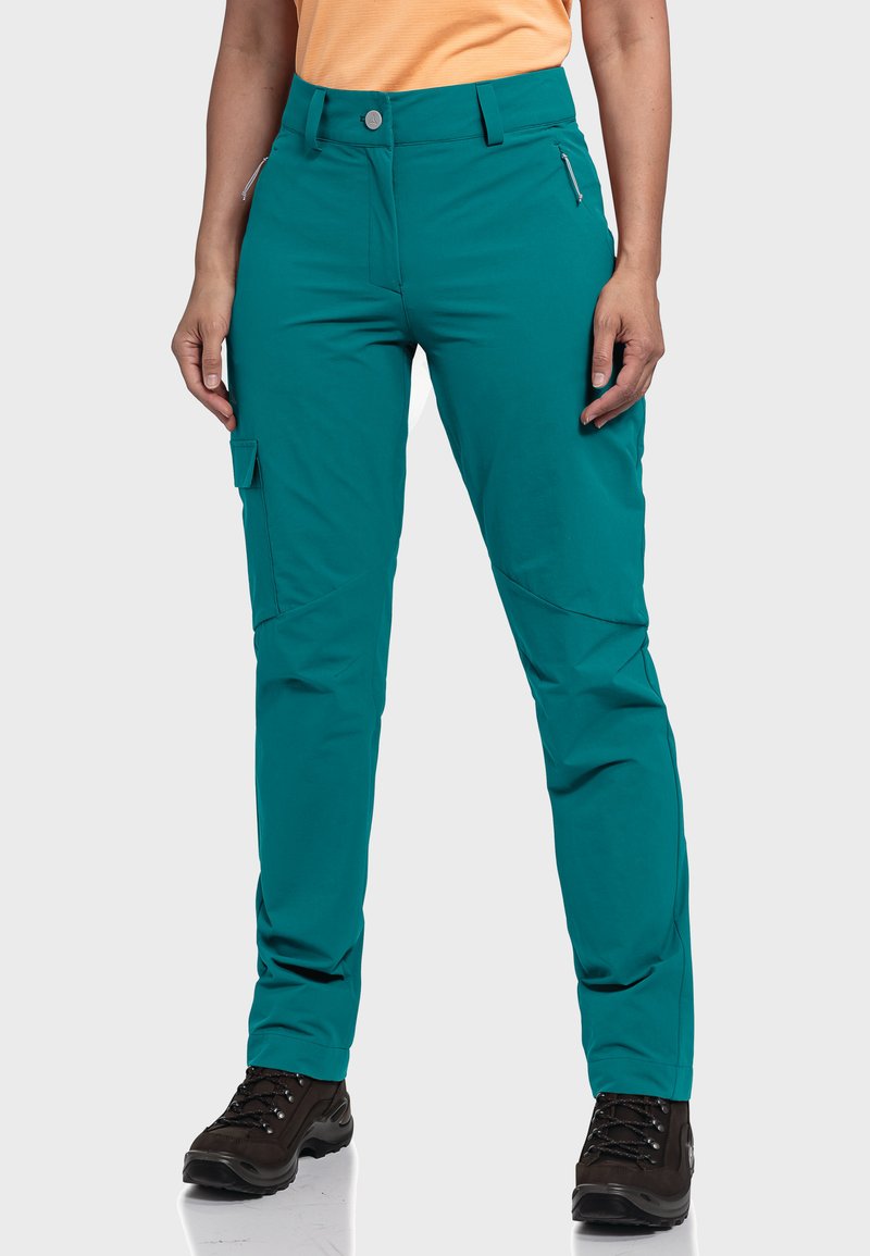 Türkisfarbene Wandershorts aus leichtem Material, mit einer Reißverschlusstasche, einer Cargo-Tasche und einem entspannten Schnitt. Kombiniert mit dunklen Wanderschuhen.