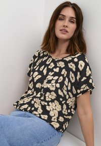 Black top with light beige floral pattern, loose fit, round neckline, and short sleeves, paired with blue jeans. Soft texture.