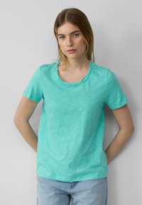 T-shirt turquoise à manches courtes en tissu doux et l�éger avec un col rond et une texture subtile, associé à un jean bleu clair.