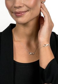 Silver infinity necklace and bracelet featuring clear accents, displayed against a black top. Sleek design with delicate chain.