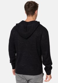 Sudadera negra de punto con una tela texturizada, que presenta una gran capucha, puños y dobladillo acanalados, vista desde atrás.
