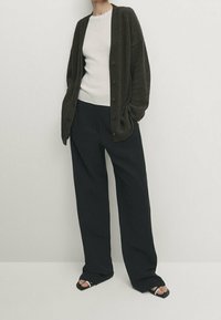 Tummanvihreä neulottu neuletakki valkoisen ribbineuletopin päällä, yhdistettynä löysiin mustiin housuihin ja mustiin remmihin. Rentoa istuvuutta, napitettava suljenta.