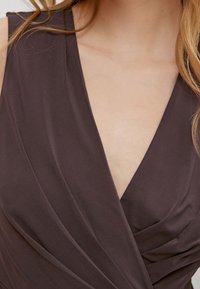 Robe marron foncé sans manches avec un décolleté plongeant en V et un détail de tissu froncé, présentant une texture lisse et des lignes épurées.