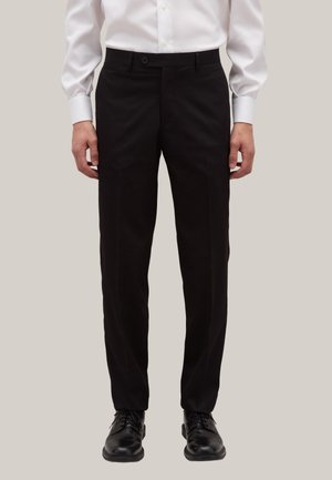Schwarze maßgeschneiderte Hosen mit flachem Bund, ausgestattet mit einem Knopfverschluss und Gürtelschlaufen. Getragen mit einem weißen Hemd und schwarzen Schuhen.