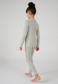 Maglietta grigia a maniche lunghe e leggings abbinati in tessuto morbido ed elasticizzato. La maglietta ha un collo rotondo e maniche aderenti, senza motivi prominenti.