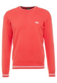 Roter Rundhals-Pullover aus Strickstoff. Mit weißen Streifen an den Bündchen und dem Saum. Kleines weißes Logo auf der Brust. Lange Ärmel.