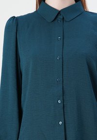 Teal overhemd met kraag, met lange mouwen en gathered accenten op de schouders. Glad textuurstof en bijpassende knopen.